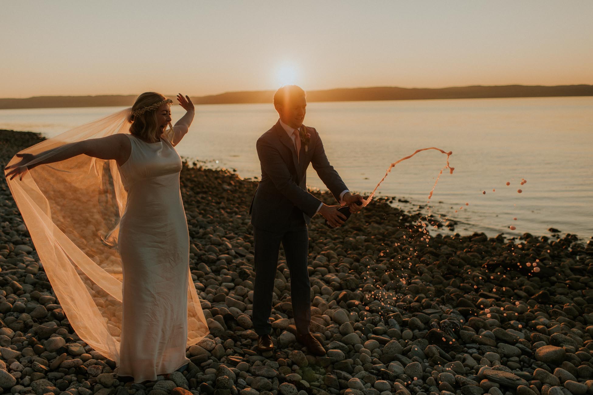 bride and groom popping champagne on beach at sunset 