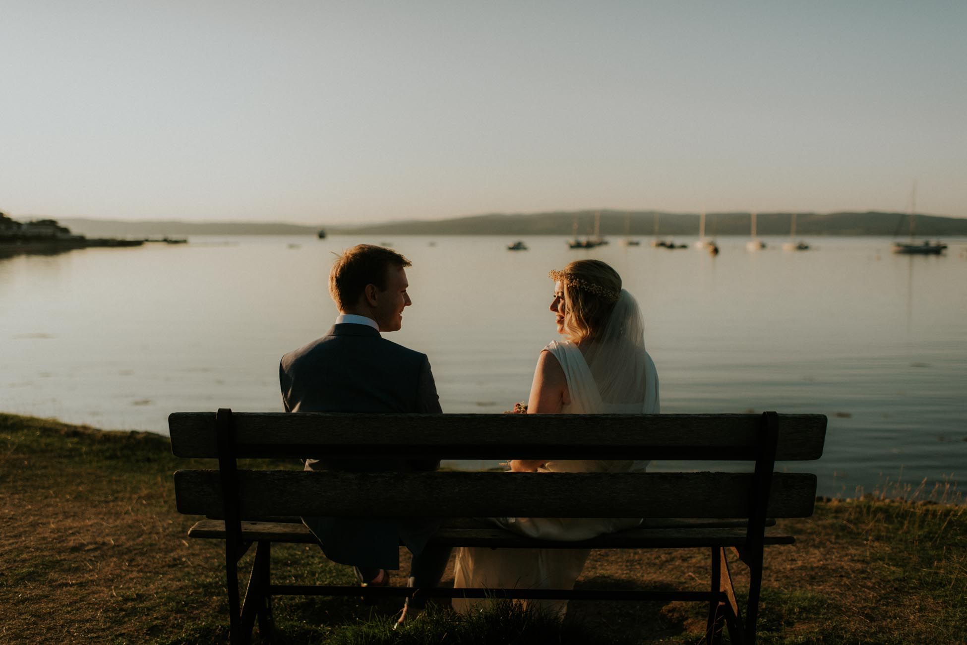 bride and groom sitting on a bench at sunset