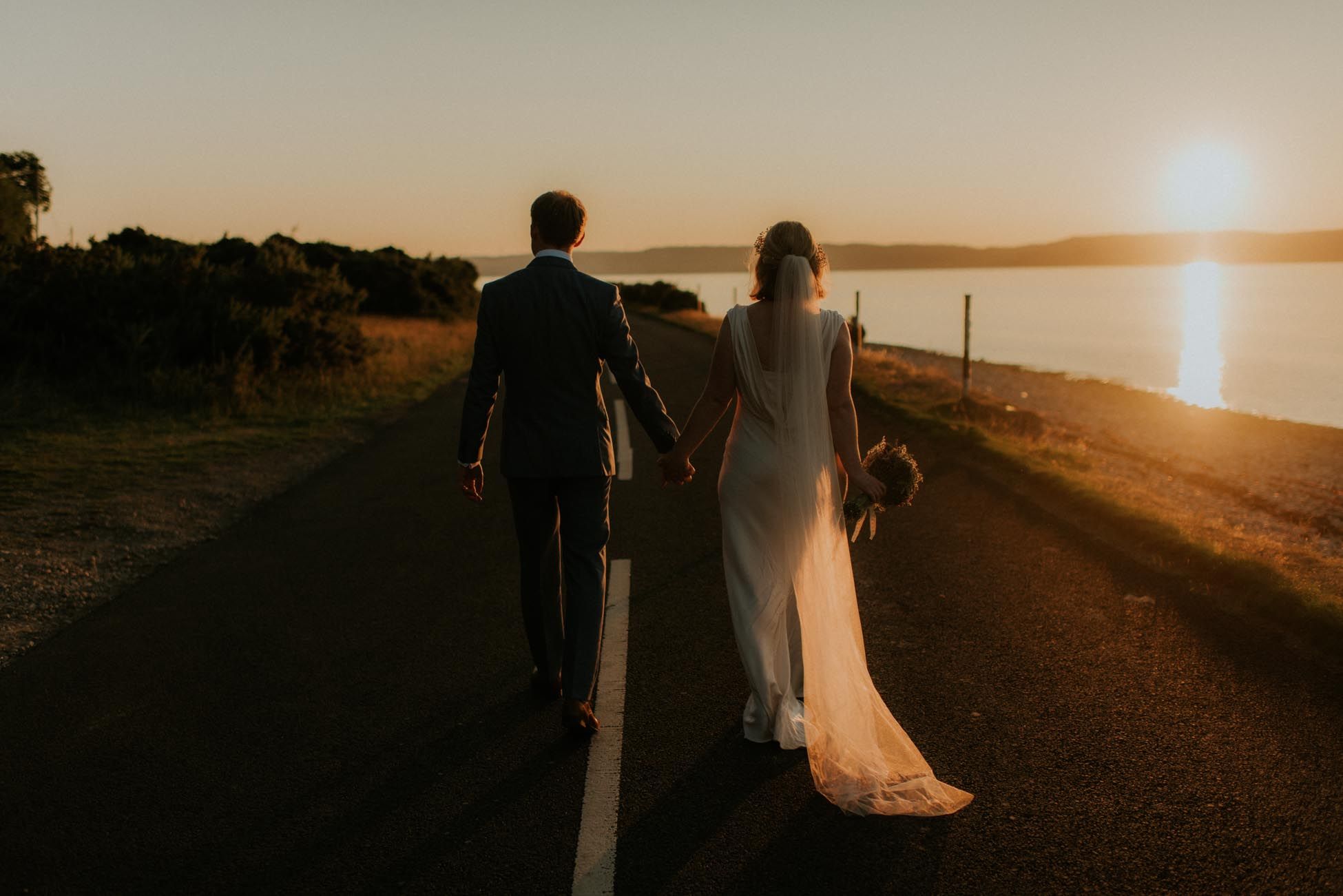 bride and groom walking along road at sunset