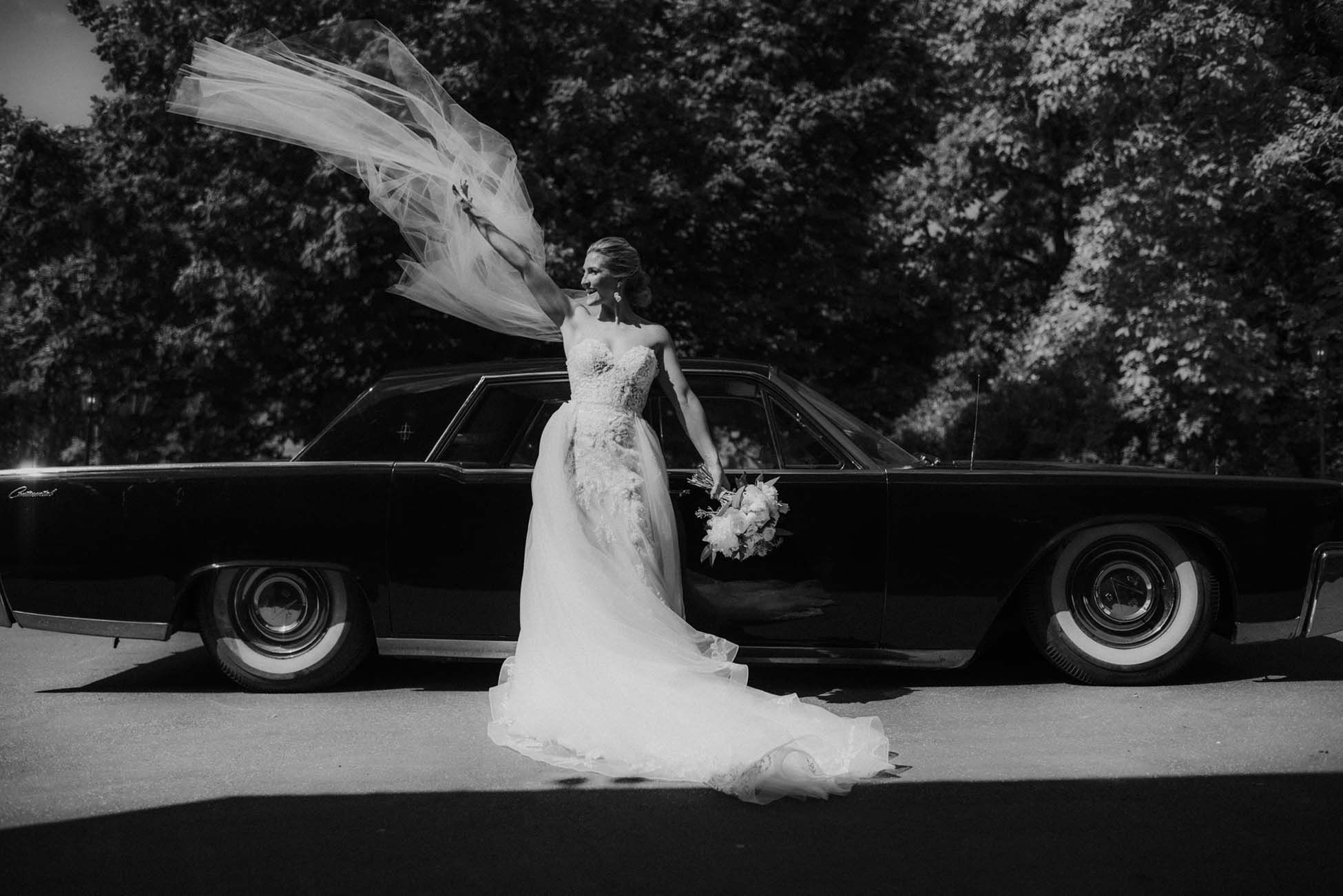 bride throwing veil in the air in front of car