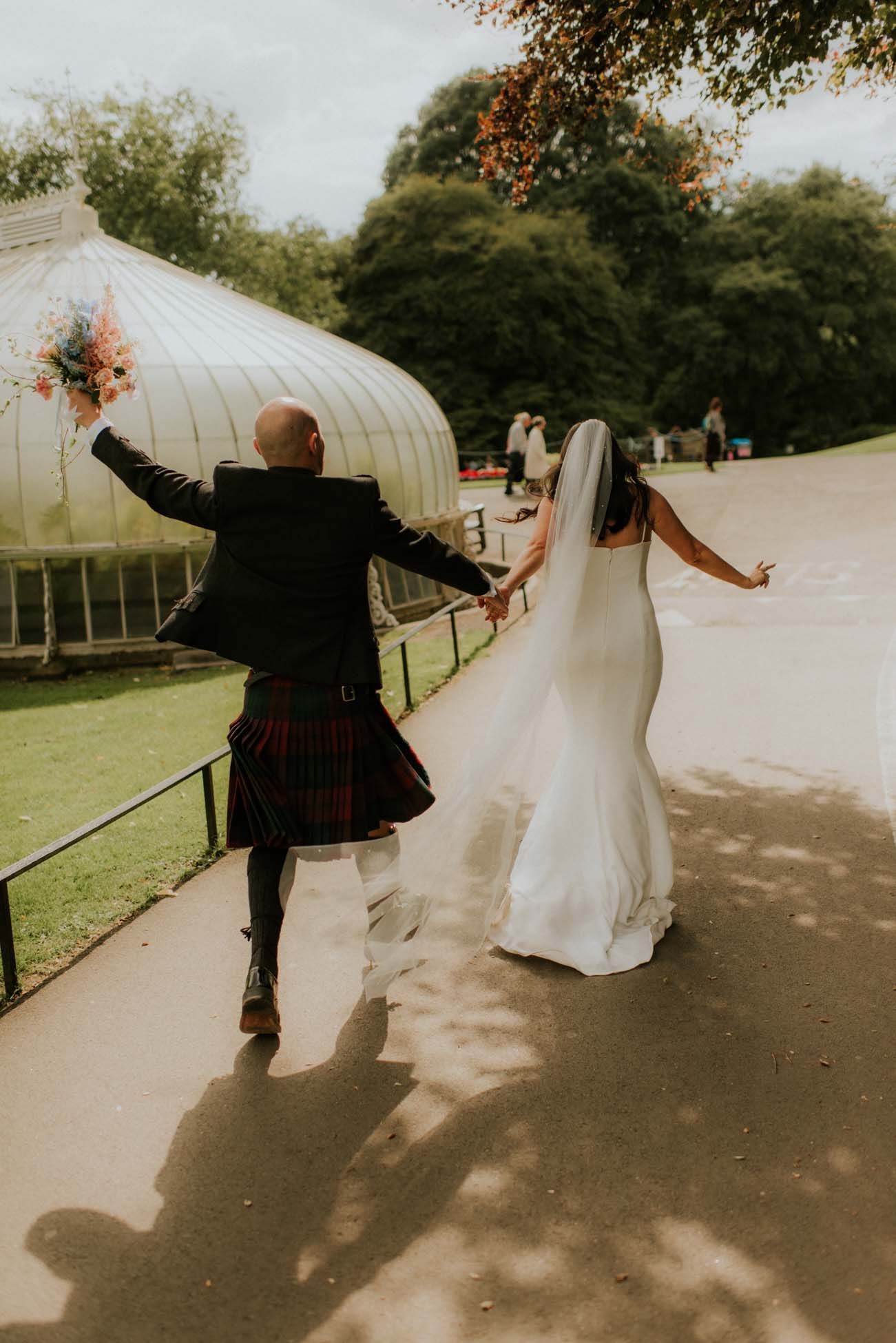 bride and groom running through Glasgow botanical gardens 